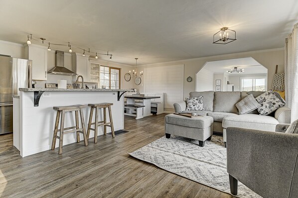A spacious living area with a kitchen, a gray sofa set, and a wooden floor.