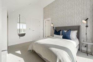 A modern bedroom with a large bed, a round mirror, and two bedside lamps. - Modern Home with Stunning Gannel Estuary Views (Newquay)