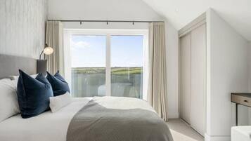 A bedroom with a large bed, a nightstand, a lamp, and a view of the outdoors through a sliding door.