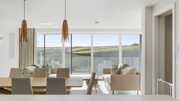 A modern dining area with a large table and chairs, large windows offering a view of the countryside.
