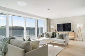 A modern living room with a sofa, coffee table, and a TV on a stand. - Modern Home with Stunning Gannel Estuary Views (Newquay)
