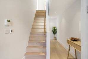 A staircase with wooden steps leading upwards, a potted plant on the landing, and a wooden table with a bowl on the right. - Modern Home with Stunning Gannel Estuary Views (Newquay)