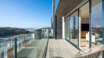 A modern balcony with glass railings overlooking a coastal landscape.