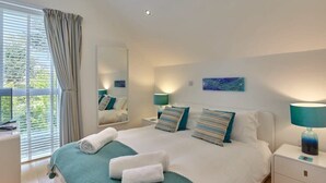 Un dormitorio moderno con una cama grande, dos mesitas de noche, un espejo y una ventana con cortinas.