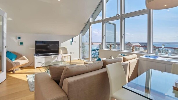 Un salón moderno con televisor grande, asientos cómodos y vista al mar.