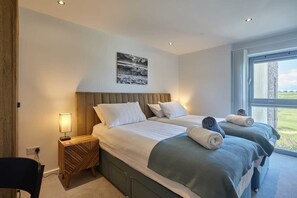 Une chambre d’hôtel avec deux lits, une table de chevet avec une lampe, un tableau au mur et une grande fenêtre donnant sur l’extérieur.
