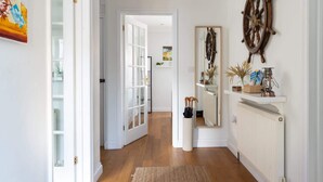 A hallway with a wooden floor, white walls, a large mirror, and a ship's wheel decoration.