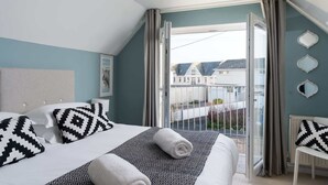 A bedroom with a bed, a chair, a window, and a view of houses outside.