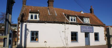 A two-story building with a tiled roof, a sign reading "Stiffkey Red Lion," and a small porch area.
