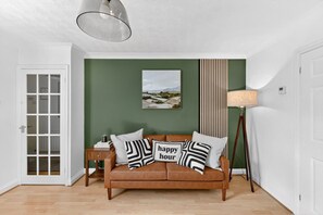 Una habitación con un sofá de cuero marrón, una mesita auxiliar, una lámpara, un cuadro enmarcado y una puerta con paneles de vidrio.
