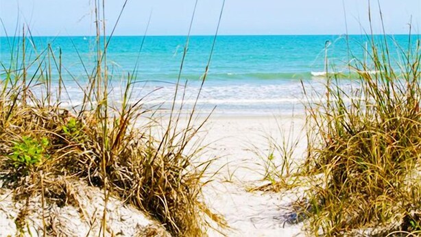 A beach with sand and grass in the foreground and a clear blue ocean in the background. - Cape Canaveral Charm Double Wide Patio & Heated Amenities (Cape Canaveral)