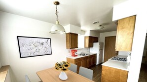 Una cocina compacta con armarios de madera, una encimera blanca y un comedor con mesa y sillas.