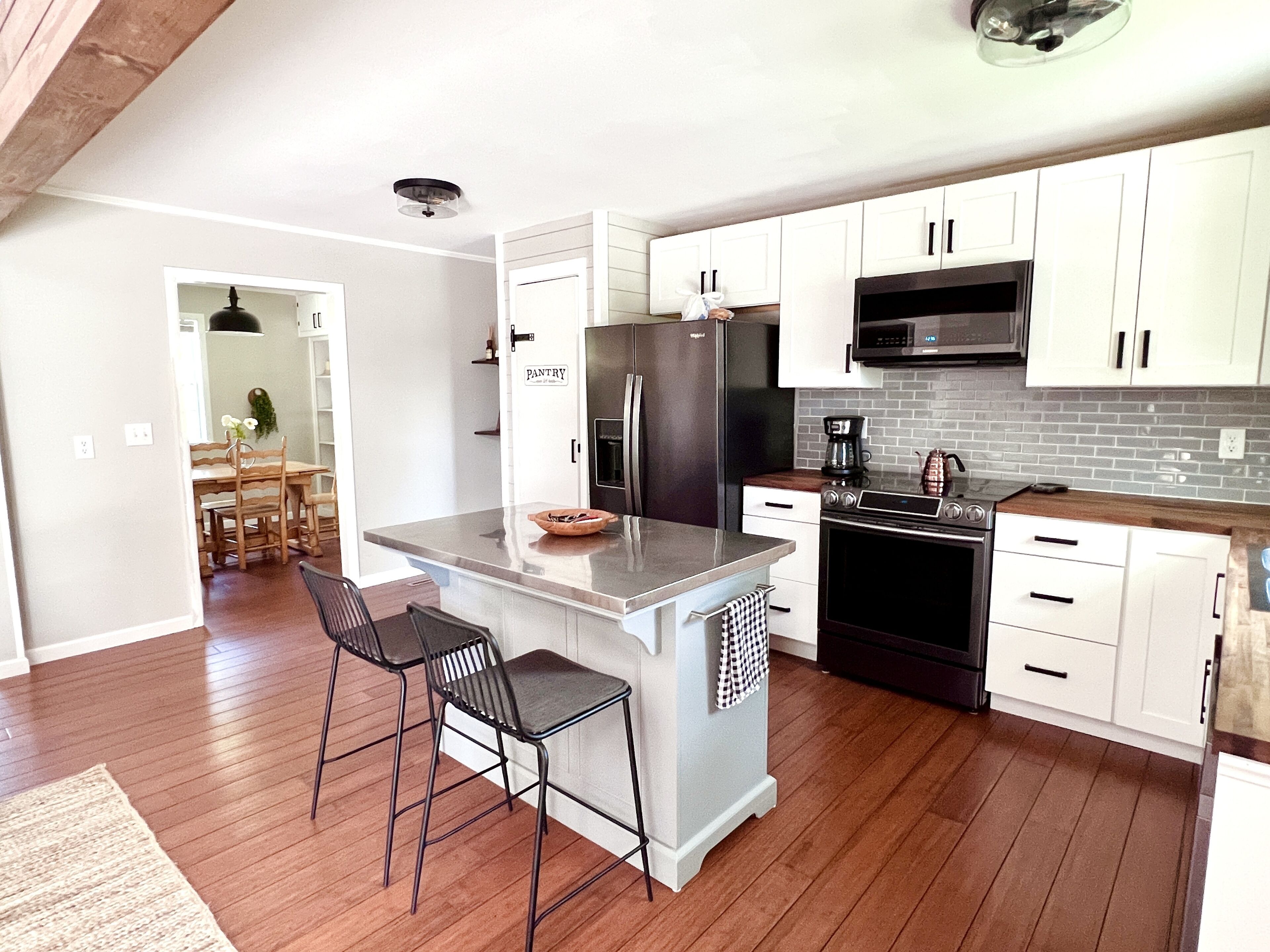 Una cocina moderna con armarios blancos, un refrigerador negro, un microondas y una cafetera.