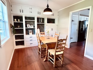 A dining area with a wooden table and chairs, white cabinets, and a hanging light fixture.