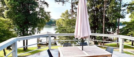 A deck with a table and chairs, overlooking a lake with trees and a dock in the background.
