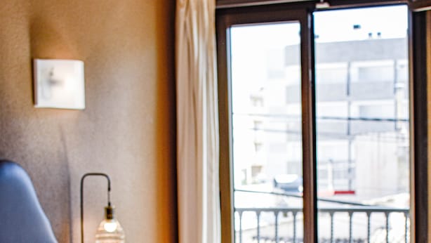 Hotellihuone, jossa on kaksi sänkyä, yöpöytä lampun kanssa ja näkymä kaupunkiin ikkunasta.