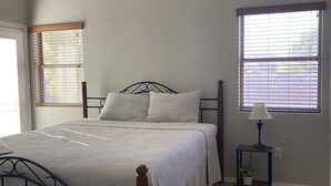 A bedroom with a bed, a ceiling fan, a window with blinds, and a nightstand with a lamp. - SummerHaven 5 minute drive to river (Mohave Valley)