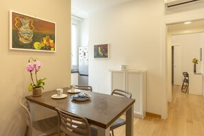 A dining area with a wooden table, chairs, a vase with flowers, and two paintings on the wall. - Pisacane Suite (Salerno)