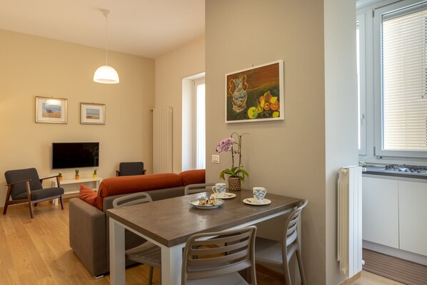 A modern living room with a dining area, a flat-screen TV, and a painting on the wall. - Pisacane Suite (Salerno)