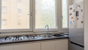 A kitchen with a stainless steel refrigerator, a gas stove, a sink, and a window with blinds. - Pisacane Suite (Salerno)