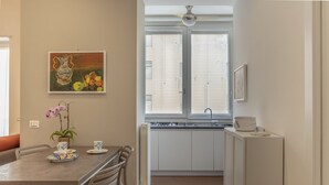 A modern kitchen with white cabinets, a dining table with chairs, and a window with blinds. - Pisacane Suite (Salerno)