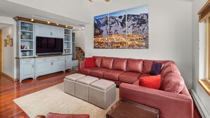 A living room with a red leather sofa, a TV, and a large mountain landscape painting. - Seasons Four by Snowmass Vacations (Snowmass Village)