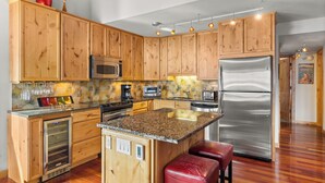 A kitchen with wooden cabinets, a granite countertop, stainless steel appliances, and a built-in wine cooler. - Seasons Four by Snowmass Vacations (Snowmass Village)