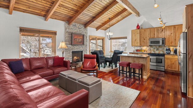 A spacious living area with a leather sofa, ottomans, a fireplace, and a kitchen with wooden cabinets and stainless steel appliances. - Seasons Four by Snowmass Vacations (Snowmass Village)