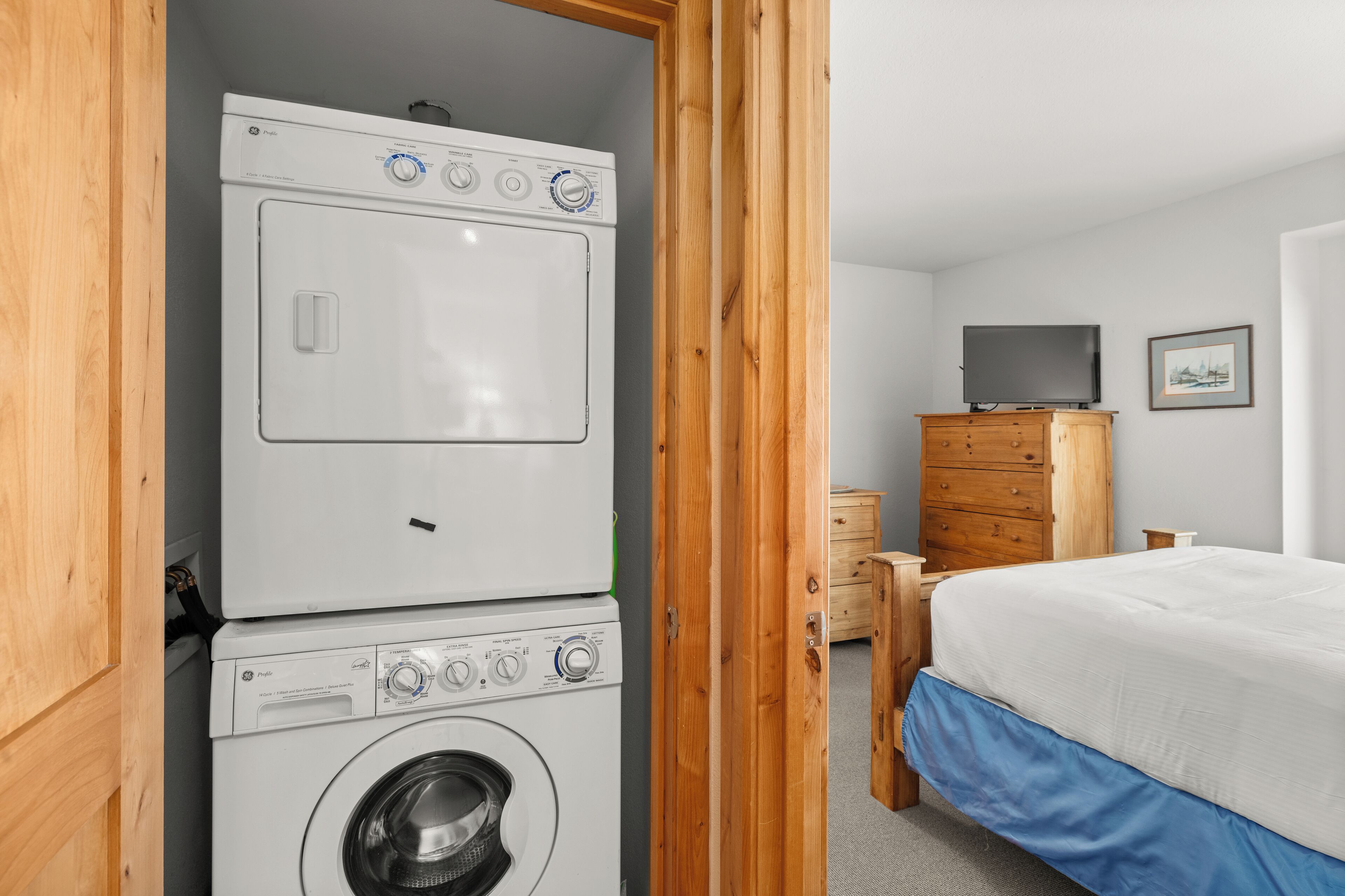 Uma lavanderia com máquinas de lavar empilhadas e um quarto adjacente com uma cama de colchão azul.