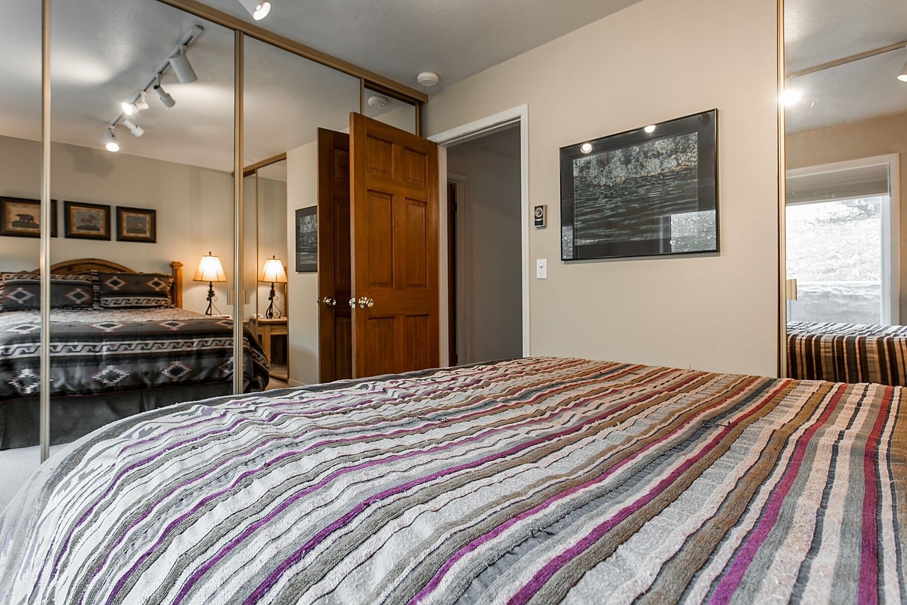 A bedroom with a large bed, a wardrobe, a mirror, and a painting on the wall.