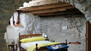 Une chambre à coucher rustique avec un lit en bois, une petite table de chevet, une lampe et une chaise pliante bleue sur laquelle sont posés des livres.