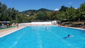 Une piscine à l’eau d’un bleu cristallin, entourée d’une terrasse carrelée et d’arbres.