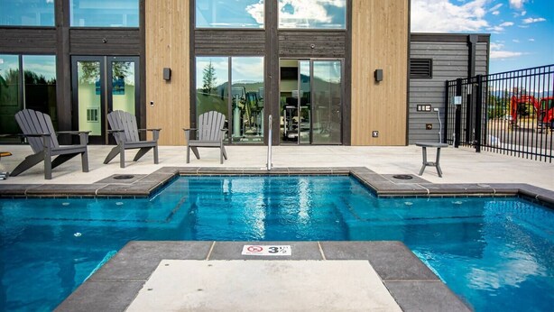 A modern building with a swimming pool, Adirondack chairs, and a fenced area. - Beautiful 2BD + 2BA Home! King Beds! Hot Tub! Pool! Walk to downtown. (Whitefish)