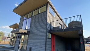 A modern two-story building with a flat roof, large windows, and a red door. - Beautiful 2BD + 2BA Home! King Beds! Hot Tub! Pool! Walk to downtown. (Whitefish)