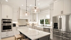 A modern kitchen with white cabinetry, stainless steel appliances, and a large island with bar stools. - Majestic Oaks, Breathtaking Sunrise Ocean Views, Shared Pool, Near the Village (St Simons Island)