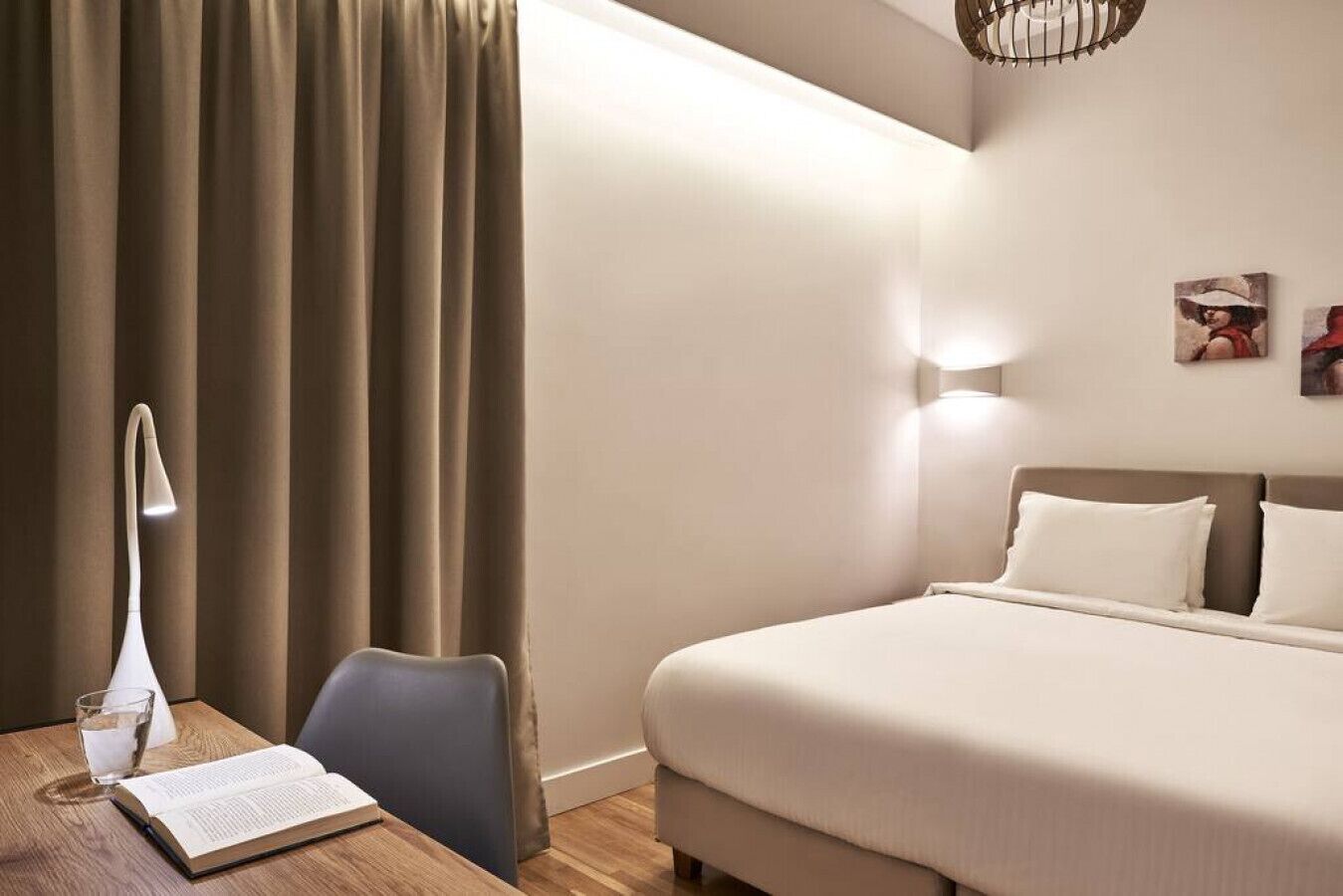 Ein Hotelzimmer mit einem Bett, einem Schreibtisch mit Lampe, einem Sessel und einem Fenster mit Vorhängen.