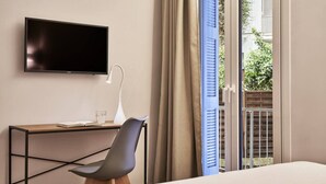 Une chambre d’hôtel moderne dotée d’une télévision à écran plat, d’un bureau avec une chaise, d’une table de chevet et offrant une vue sur un jardin grâce à une porte coulissante.