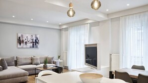 Un salon moderne avec un canapé, un coin repas comprenant une table et des chaises, un téléviseur et un îlot de cuisine avec un saladier.