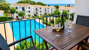A balcony with a pool, a table with wine glasses, and a view of white buildings and the sea. - Apartment with terrace, swimming pool and private parking on the Costa Brava (Palafrugell)