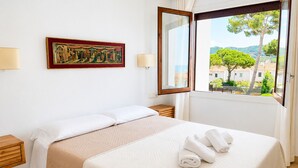 A hotel room with a bed, a window with a view, a painting on the wall, and a nightstand. - Apartment with terrace, swimming pool and private parking on the Costa Brava (Palafrugell)