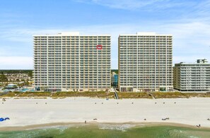 Un hôtel situé en bord de mer, composé de plusieurs immeubles de grande hauteur, avec une plage de sable fin et un ciel dégagé.