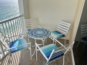 A balcony with a tiled floor, a round table with a mosaic top, and four white chairs with blue cushions. - Enjoy Breath-taking Sunsets & Endless Ocean Views at Soul Happy Majestic Beach! (Panama City Beach)