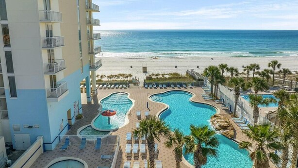 Un resort con varias piscinas, una playa y un edificio de gran altura.