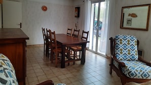 Un comedor con una mesa y sillas de madera, una araña, una puerta corredera de vidrio y un cuadro enmarcado en la pared.