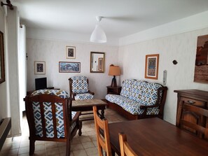 Un salon comprenant une table à manger en bois, deux canapés à motifs, un fauteuil en bois, un téléviseur et des œuvres d’art encadrées accrochées aux murs.