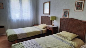 Una habitación con dos camas individuales, una mesita de noche con lámpara, un espejo y dos cuadros en la pared.