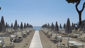 A beach with rows of sun loungers and umbrellas, a wooden walkway, and a clear view of the sea. - Hibiscus Beach Village - Apartments just a few meters from the beach. (Follonica)
