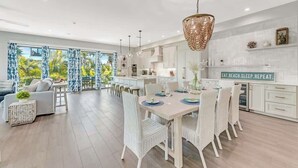 Una cocina moderna con armarios blancos, un comedor con sillas blancas y un amplio ventanal con cortinas azules.