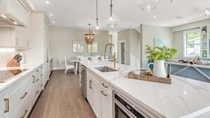Una cocina moderna con armarios blancos, encimera de mármol e iluminación colgante.