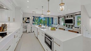 A modern kitchen with white cabinetry, a large island, and pendant lighting. - Walk to St. Armands and Lido Key Beach/Gulf Views (Sarasota)